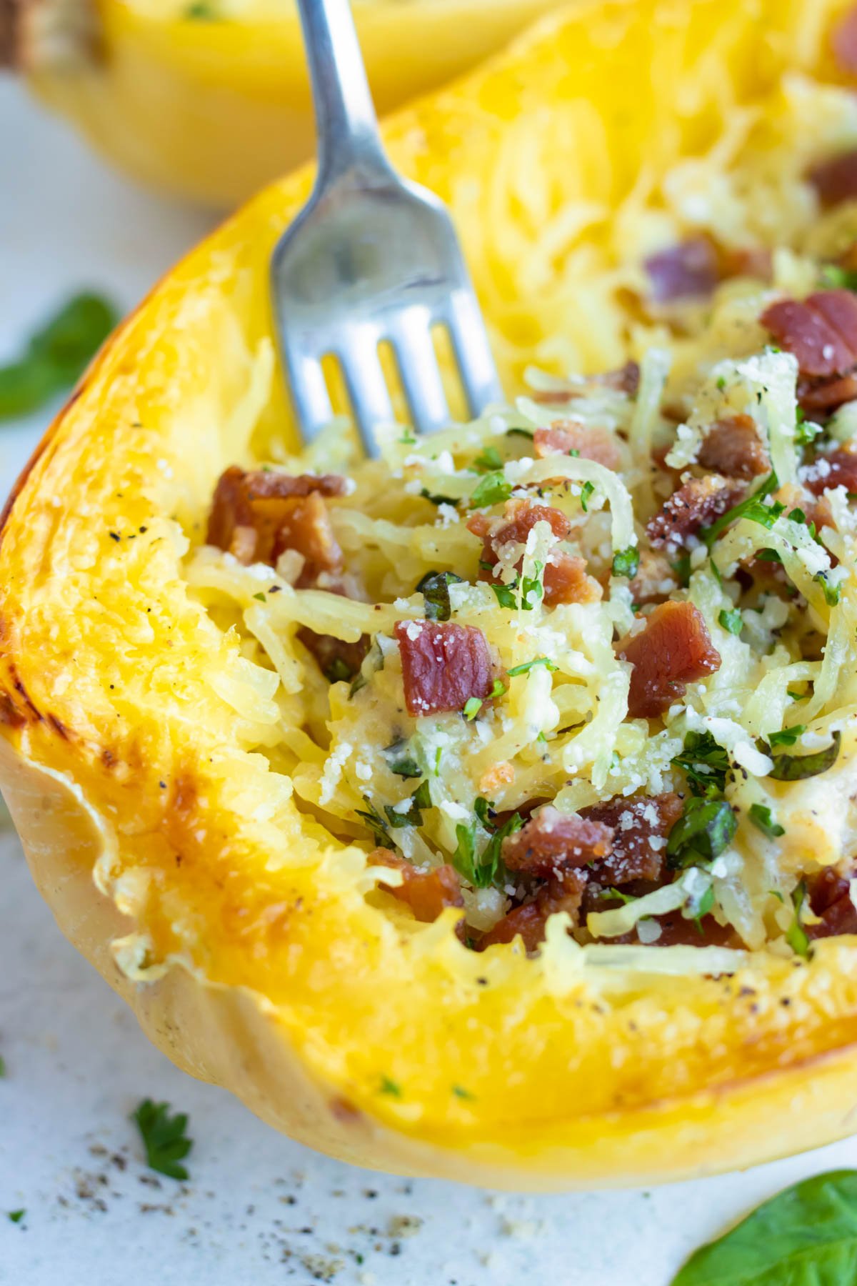 A fork digging into a Spaghetti Squash Carbonara studded with bacon.