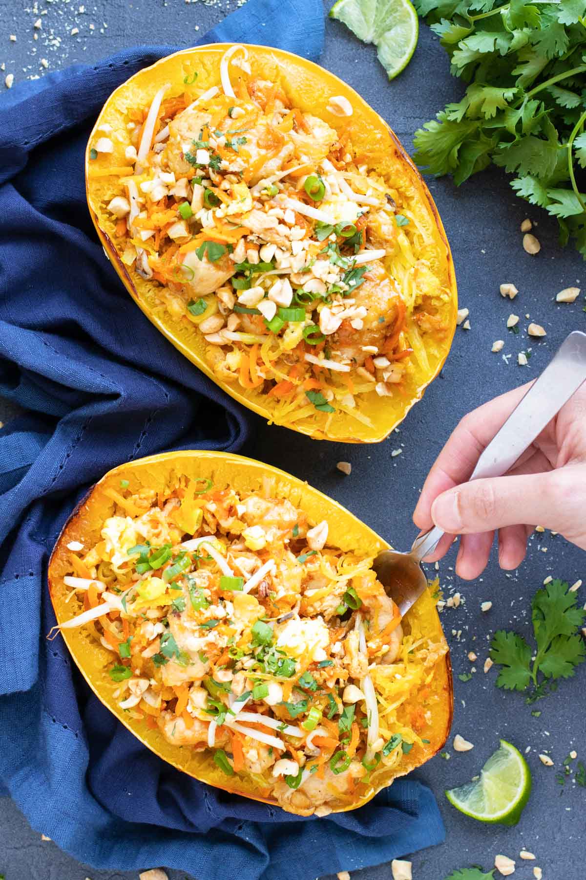 A hand with a fork inside Spaghetti Squash Chicken Pad Thai on a blue napkin and table.