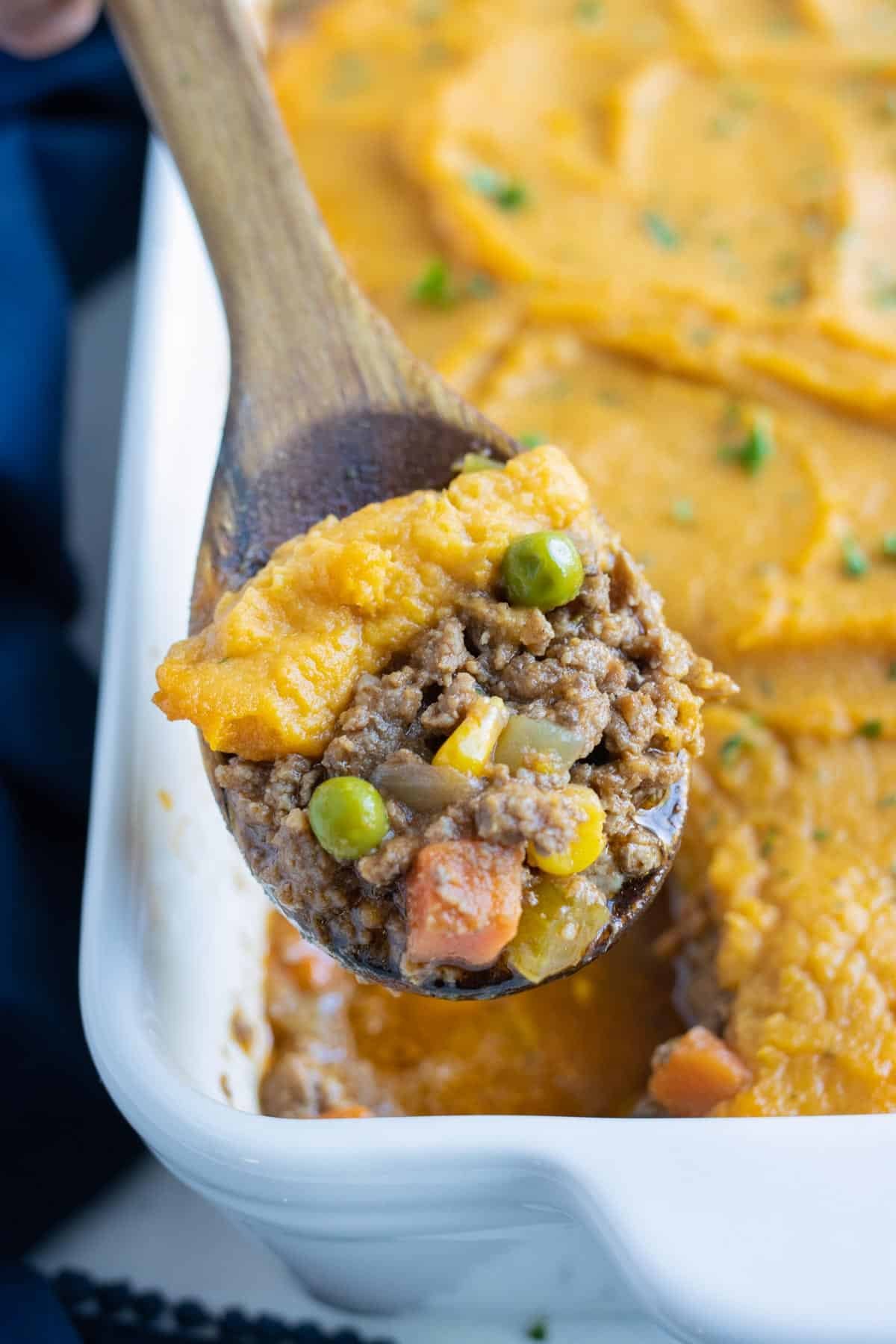 A scoop of sweet potatoes, ground beef, and veggies is served from the sweet potato casserole.