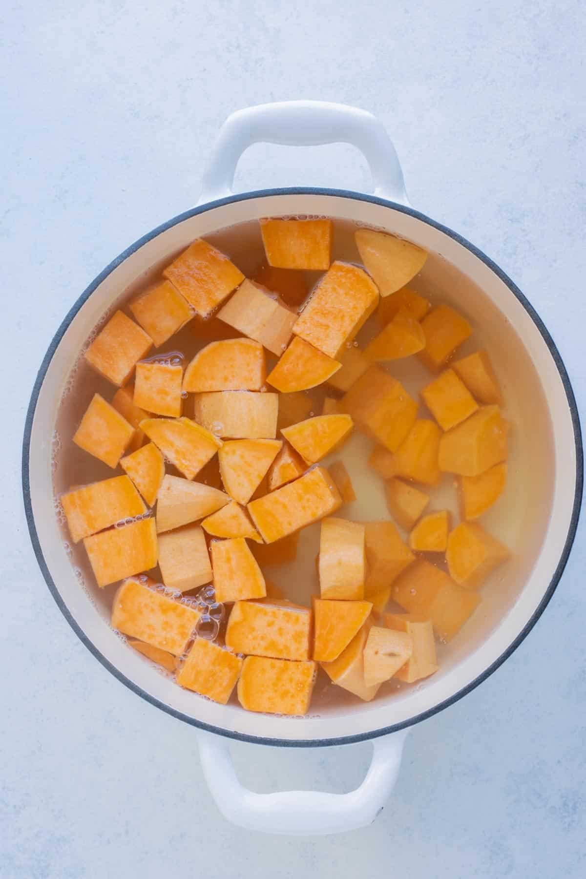 A large pot is full of boiling cubed sweet potatoes.