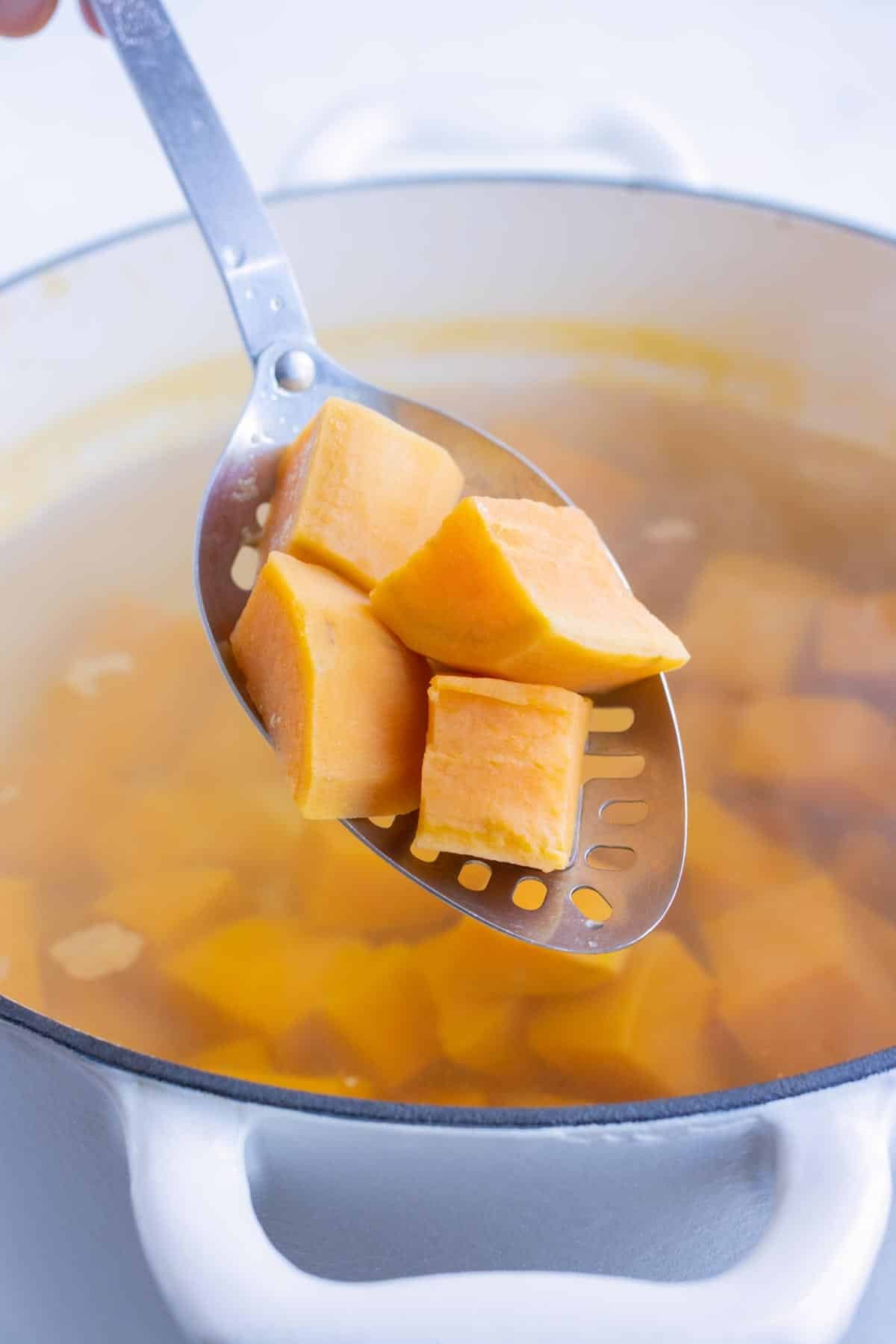 Boiled sweet potatoes are removed from the pot of boiling water.