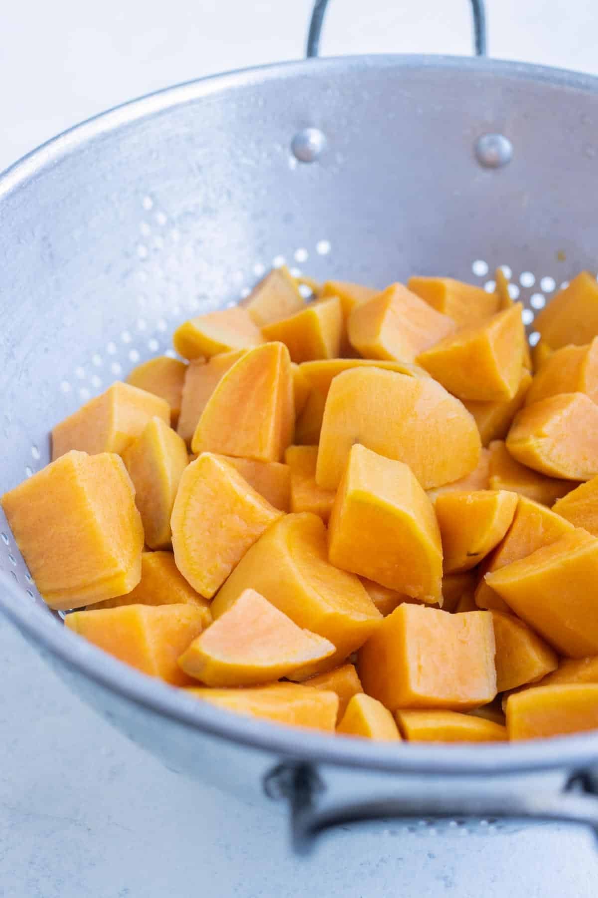 Boiled sweet potatoes are drained in a colander.