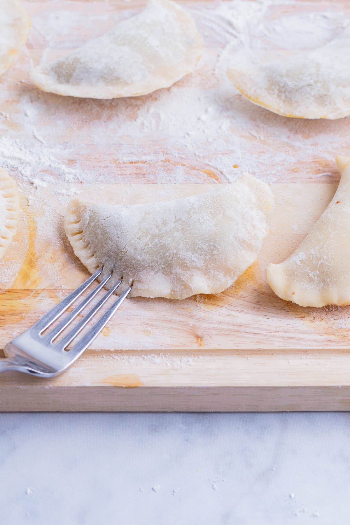 A fork crimps the edges of the empanadas.