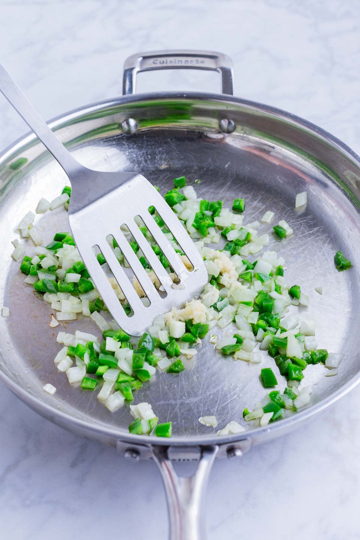 Diced onion and jalapeno sauteing in a skillet for a taco-seasoned beef empanada filling.