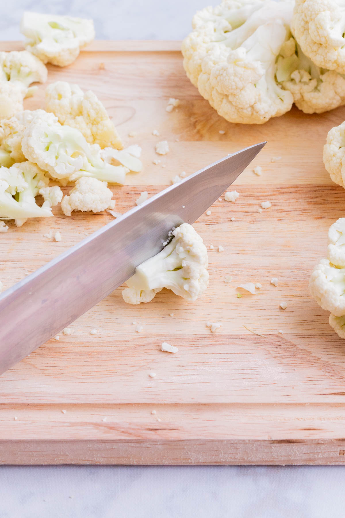 A knife cuts cauliflower into florets for a buffalo cauliflower bites recipe.
