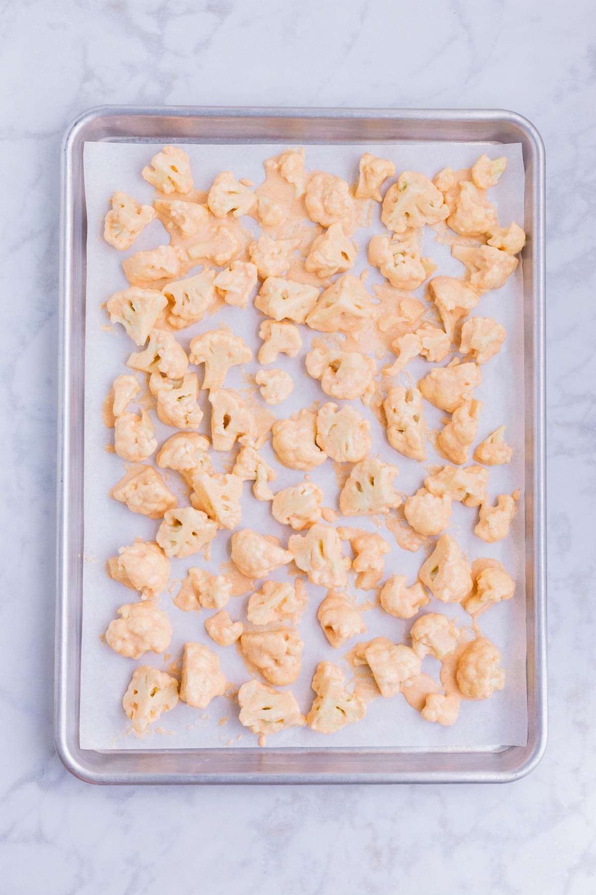 Coated cauliflower pieces are arranged on a baking sheet.
