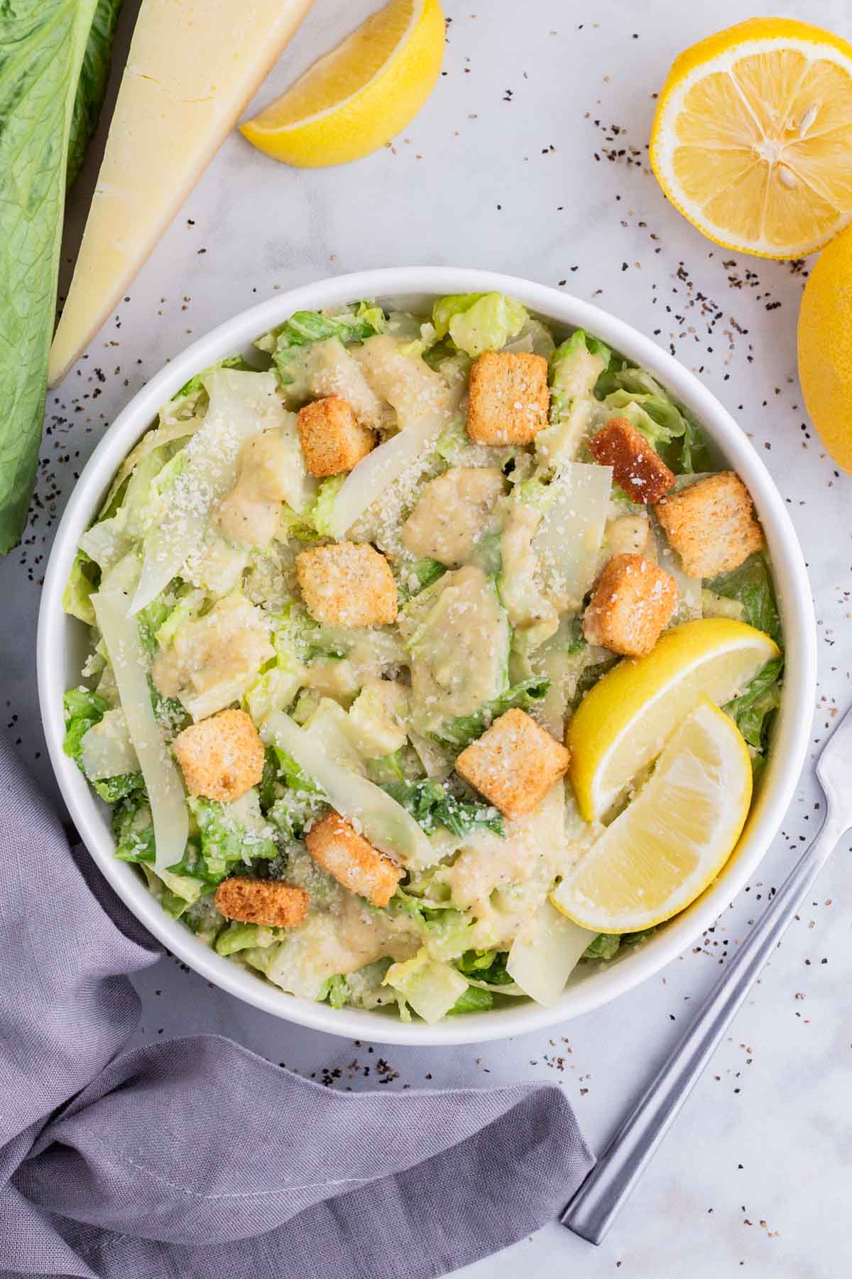 Caesar salad is topped with croutons, cheese, dressing, and a lemon.