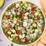 A bowl full of classic fish ceviche is made with a mix of citrus juices, avocados, tomatoes, and served with tortilla chips on the side.
