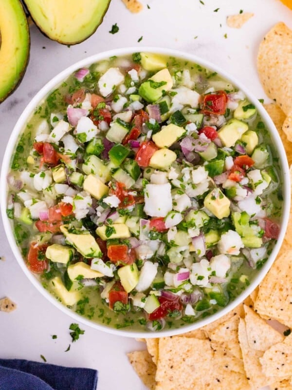 A bowl full of classic fish ceviche is made with a mix of citrus juices, avocados, tomatoes, and served with tortilla chips on the side.