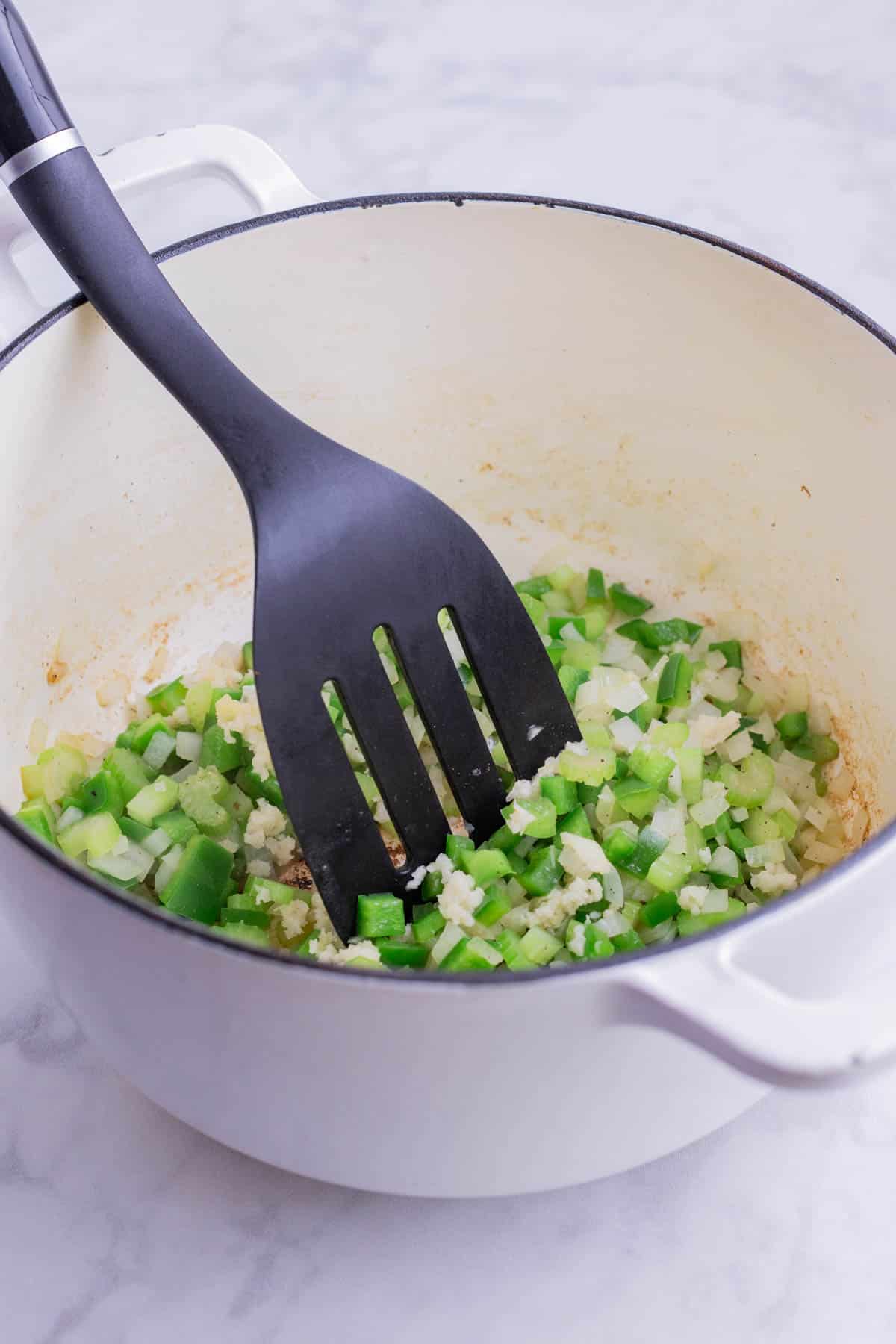 The holy trinity of onion, bell pepper, and celery is cooked in a Dutch oven.