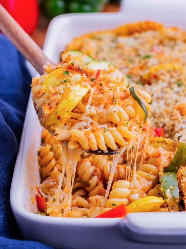 A wooden spoon scooping up baked pasta with vegetables and cheese.