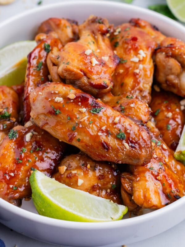 A bowl full of Thai chicken wings are served with lime wedges.