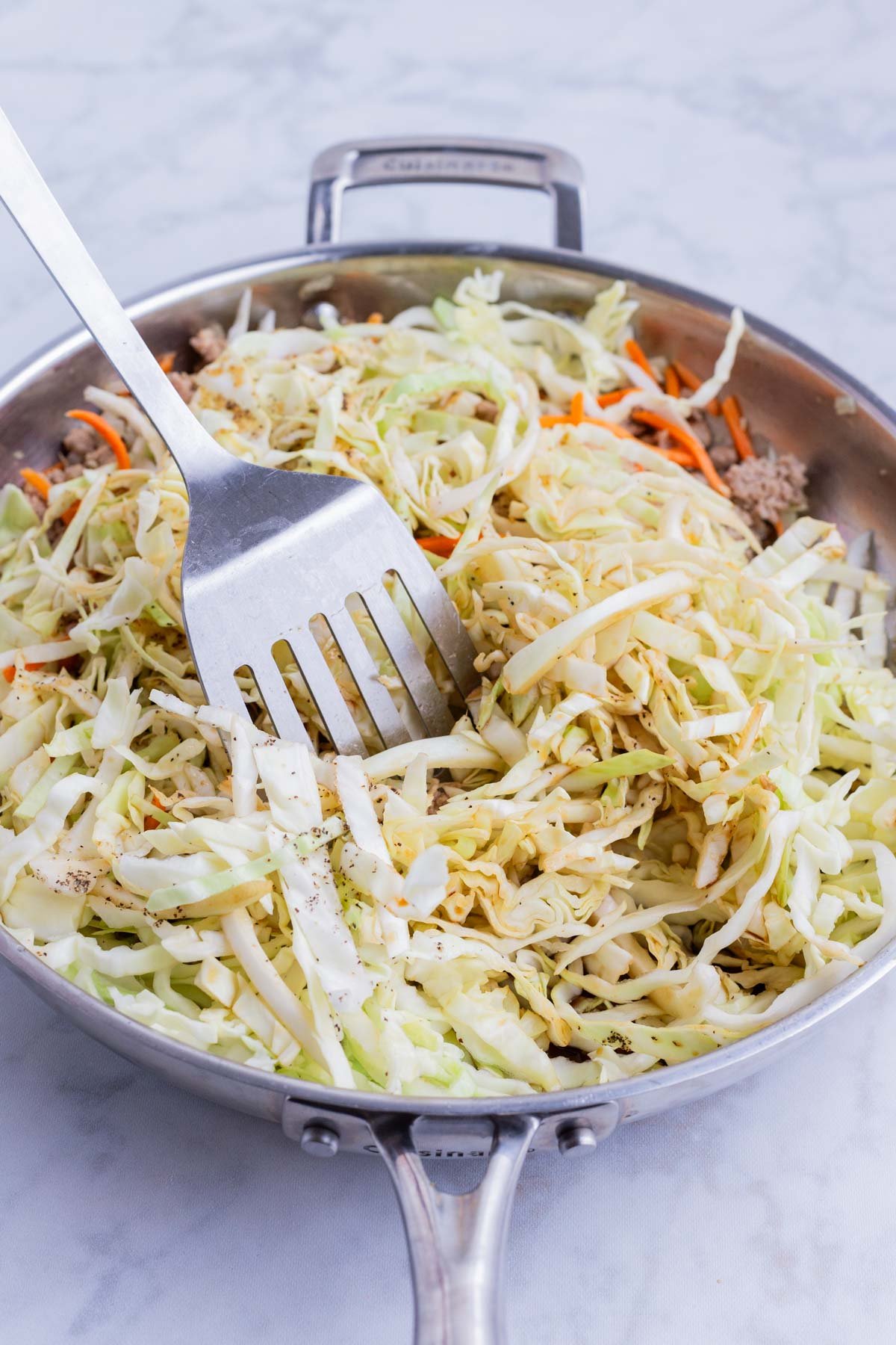 Cabbage is added to the mixture in the skillet.