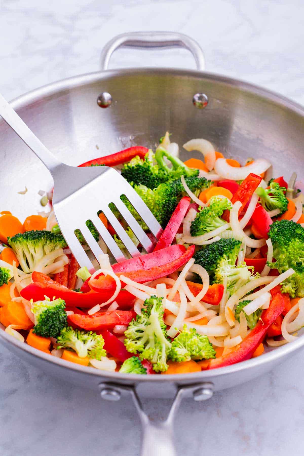 A spatula stirs fresh veggies in a skillet.