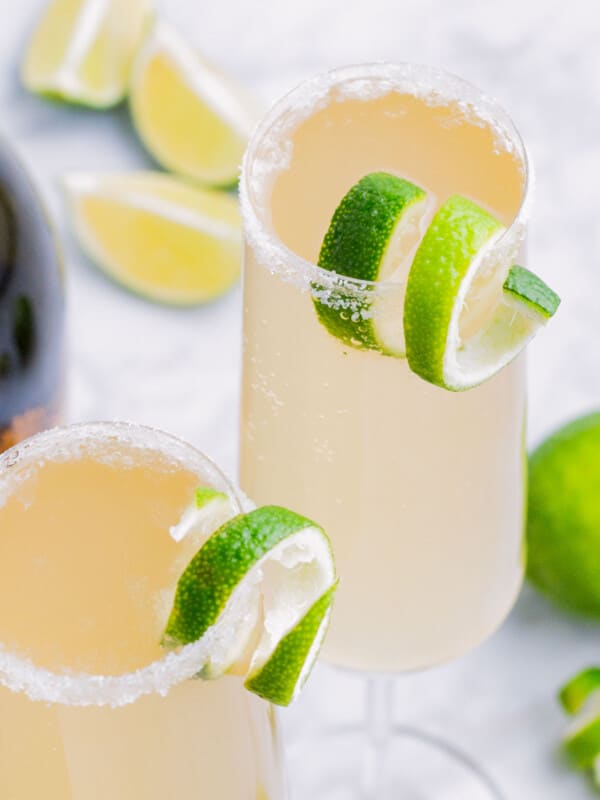 Two champagne flutes of a Mexican 75 cocktail are served with a lime.