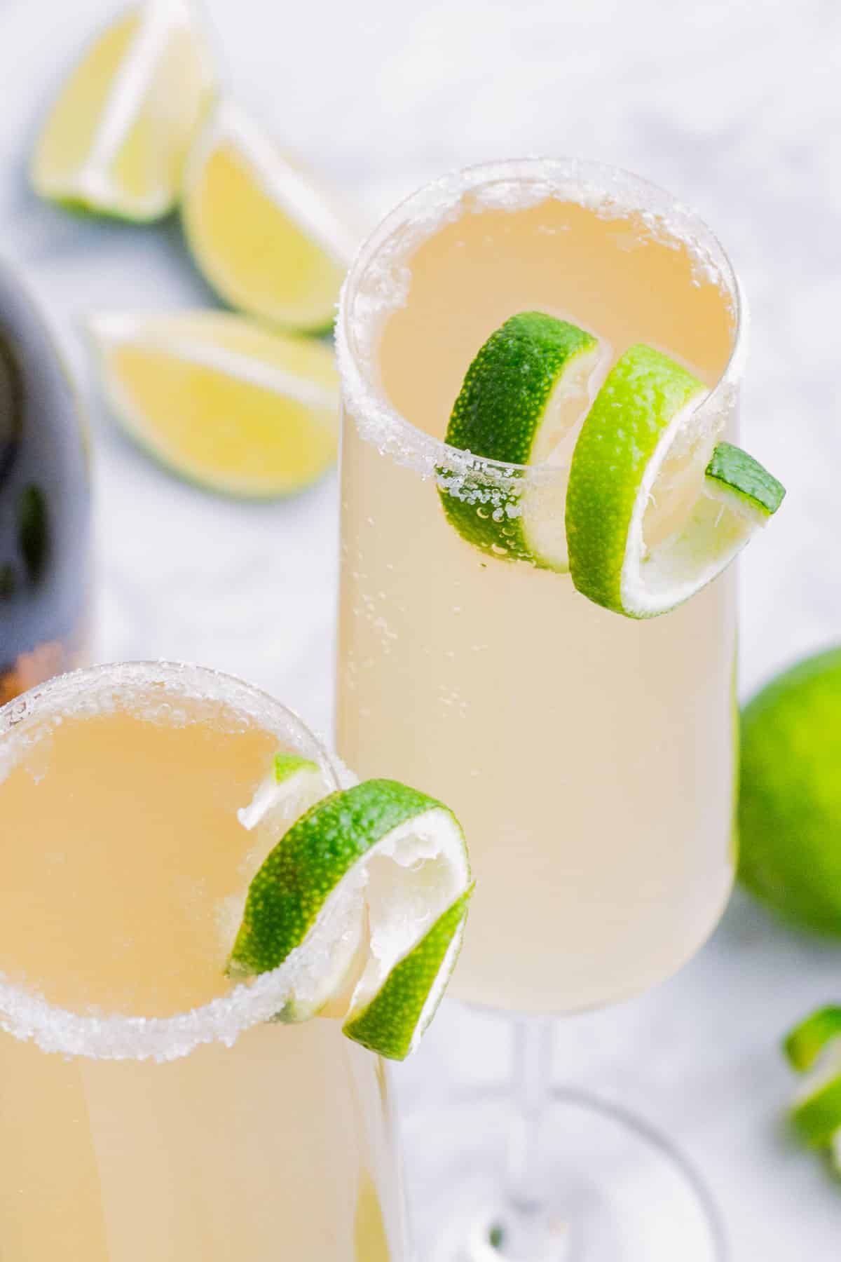 Two champagne flutes of a Mexican 75 cocktail are served with a lime.