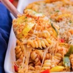 A wooden spoon scooping up baked pasta with vegetables and cheese.