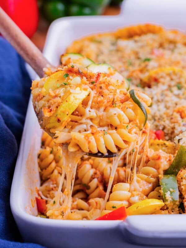 A wooden spoon scooping up baked pasta with vegetables and cheese.