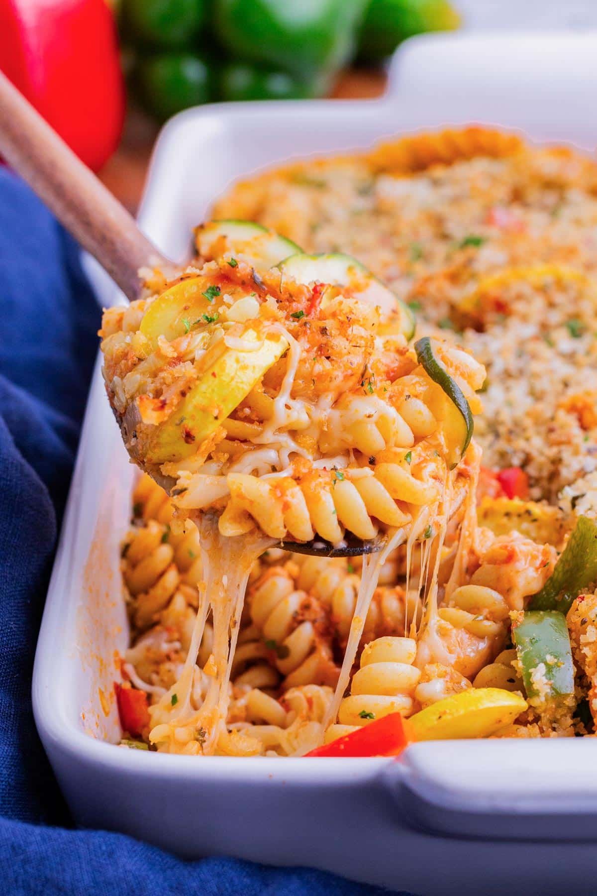 A wooden spoon scooping up baked pasta with vegetables and cheese.