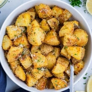 Roasted Yukon Gold Potatoes are served in a white dinner bowl with a spoon.