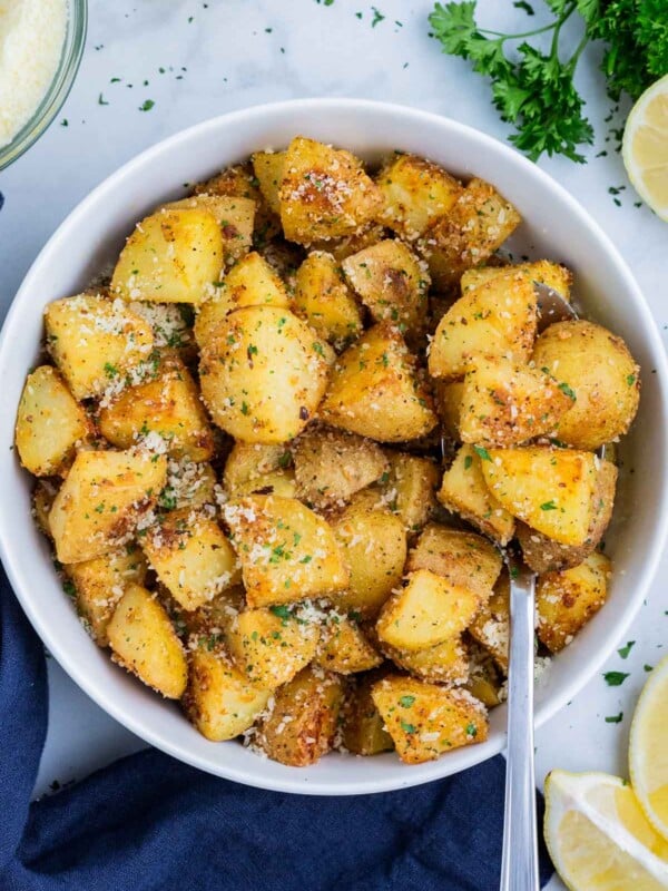 Roasted Yukon Gold Potatoes are served in a white dinner bowl with a spoon.