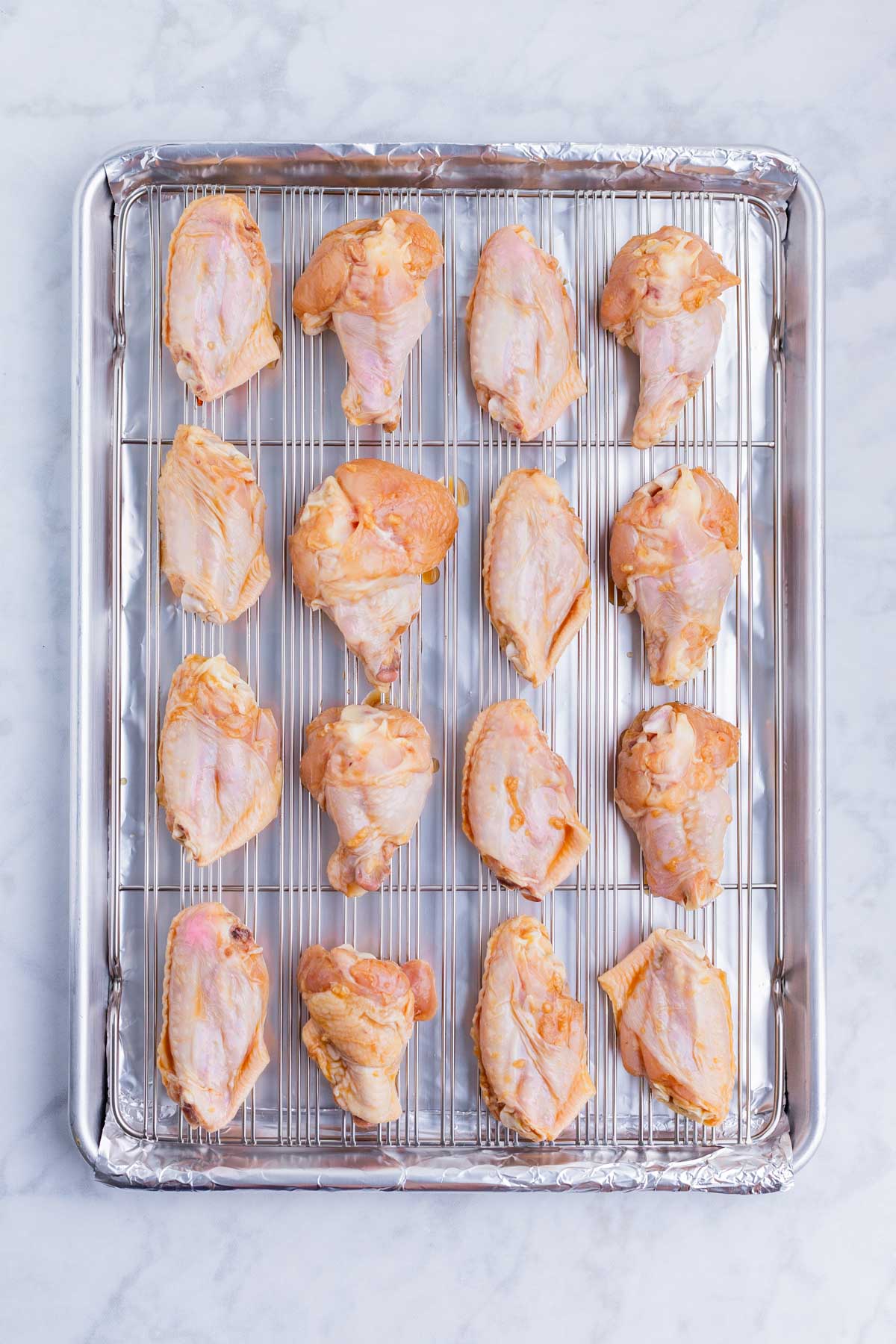 Marinated chicken wings are spread on a wired baking sheet.