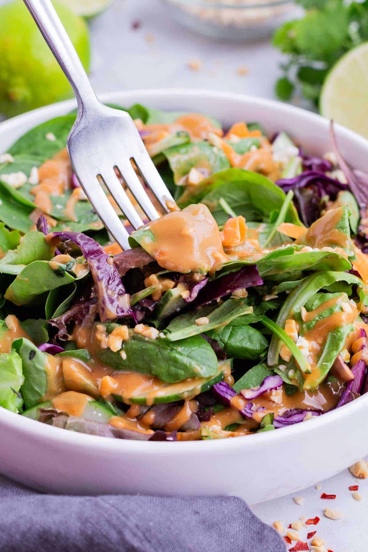A fork digs into a bowl of salad with Thai peanut sauce.