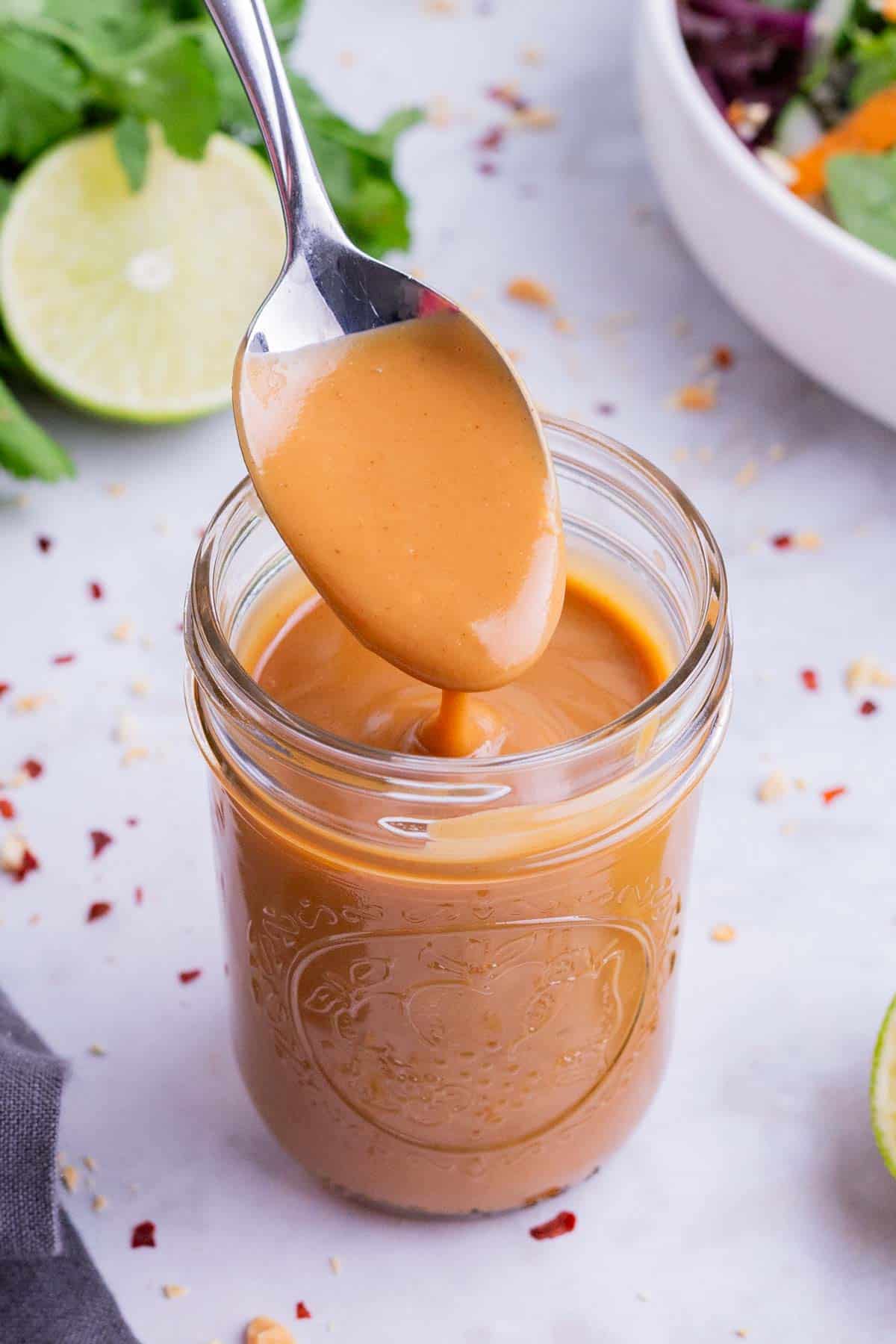 Thai peanut dressing being lifted up out of a mason jar.