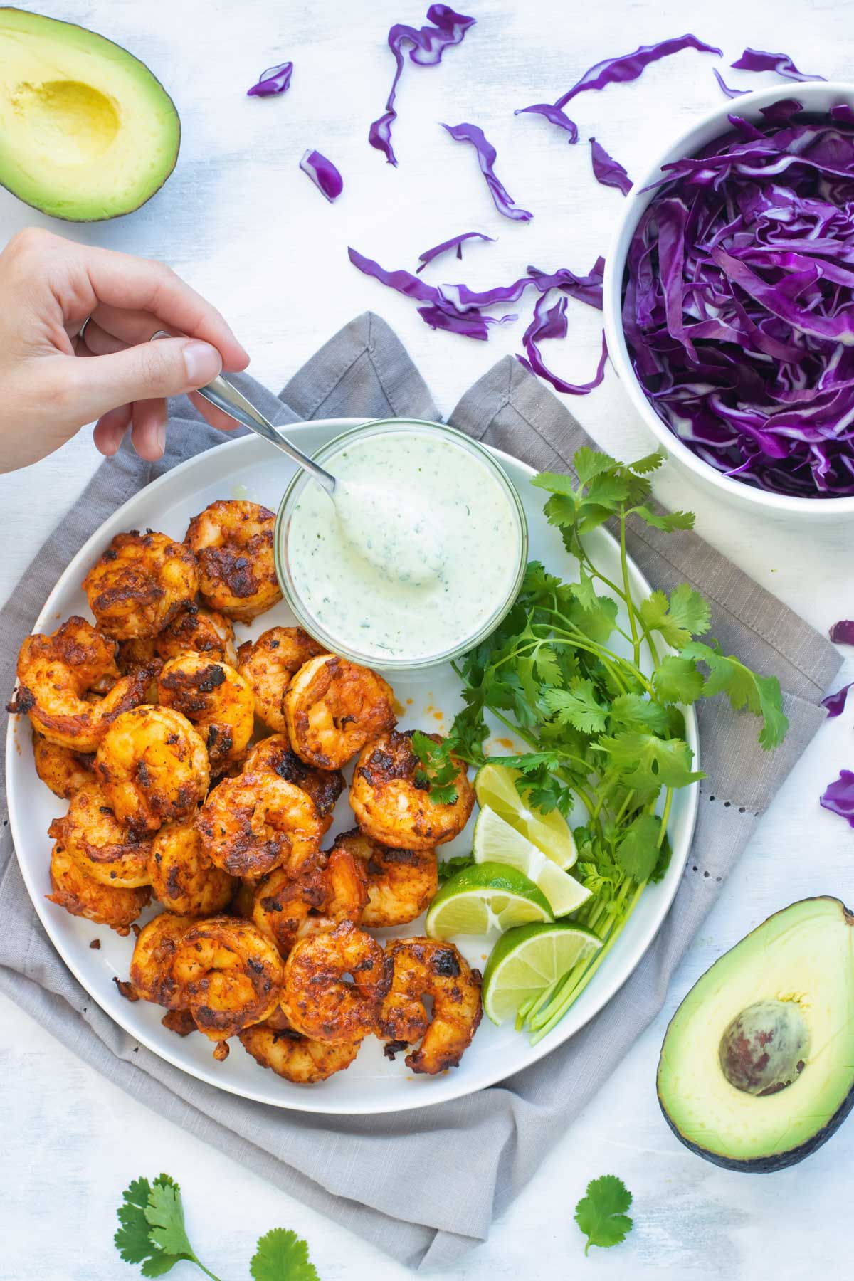 A spoon dipping into cilantro lime shrimp taco sauce on a white plate.