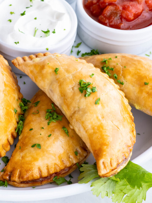 Empanadas are served on a plate with salsa, sour cream, and guacamole.