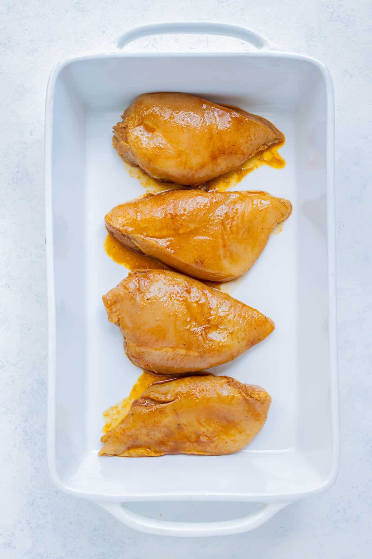 Marinated chicken breasts are laid flat in a baking dish.
