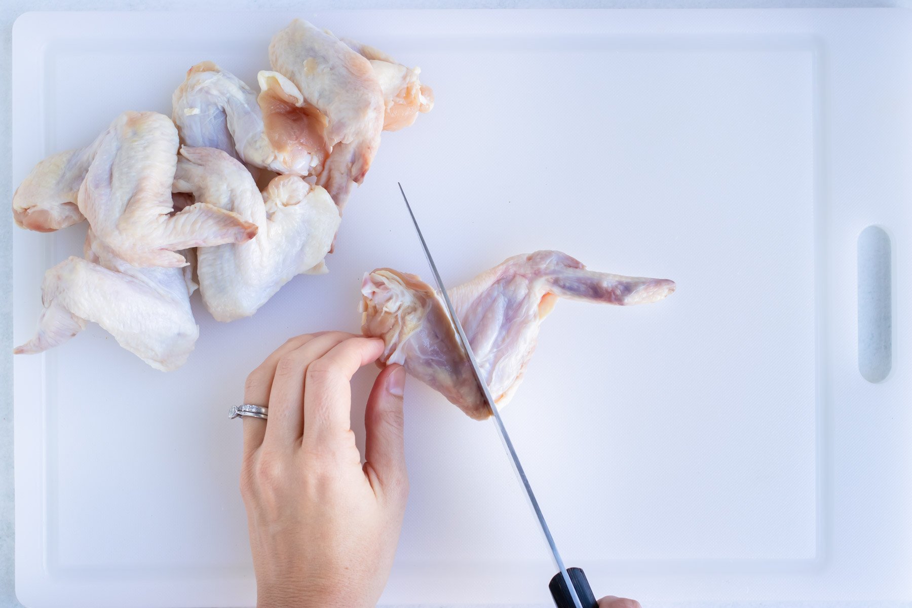 A chicken wing is cut with a knife.
