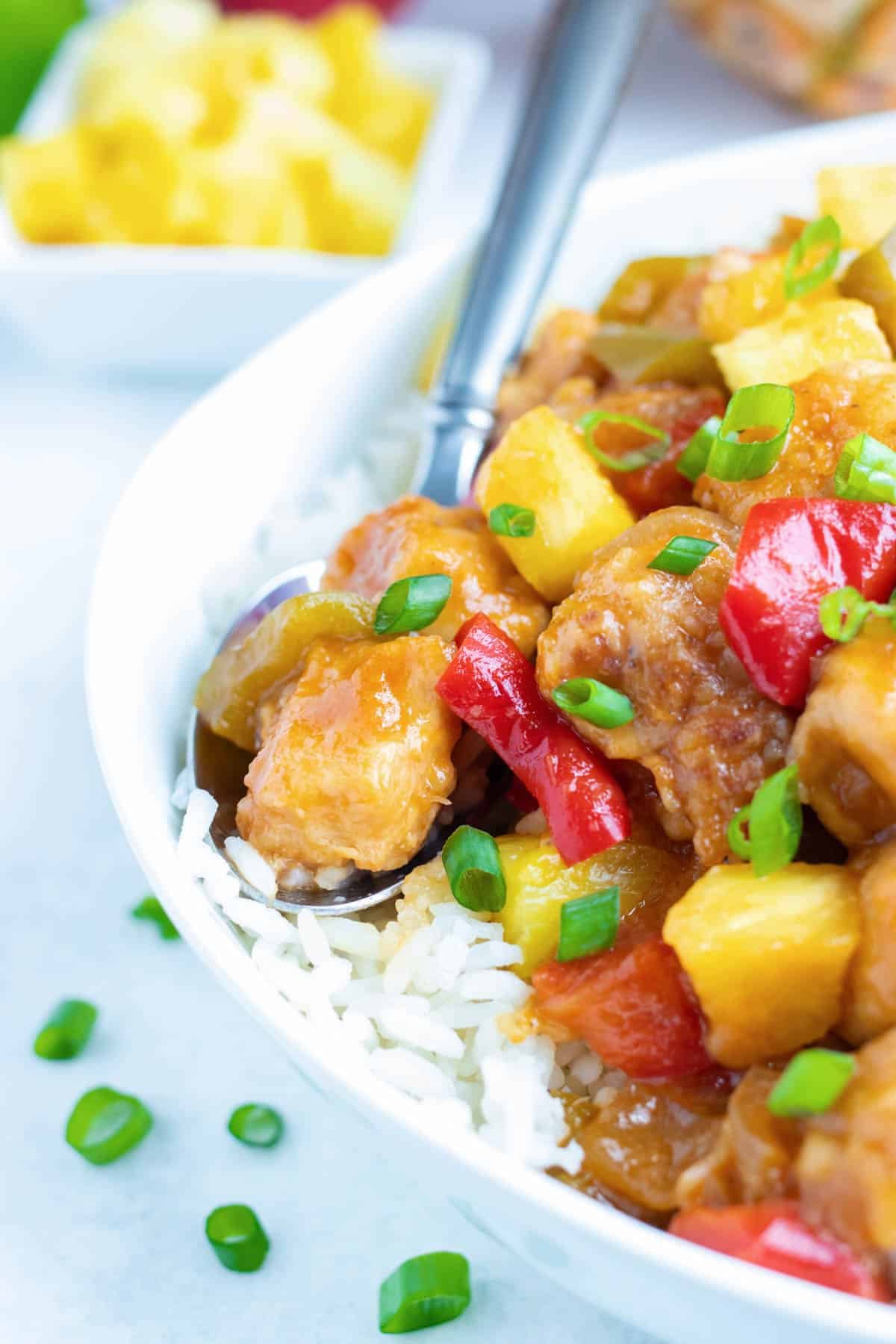 A spoonful of pineapple chicken served over rice in a white bowl.