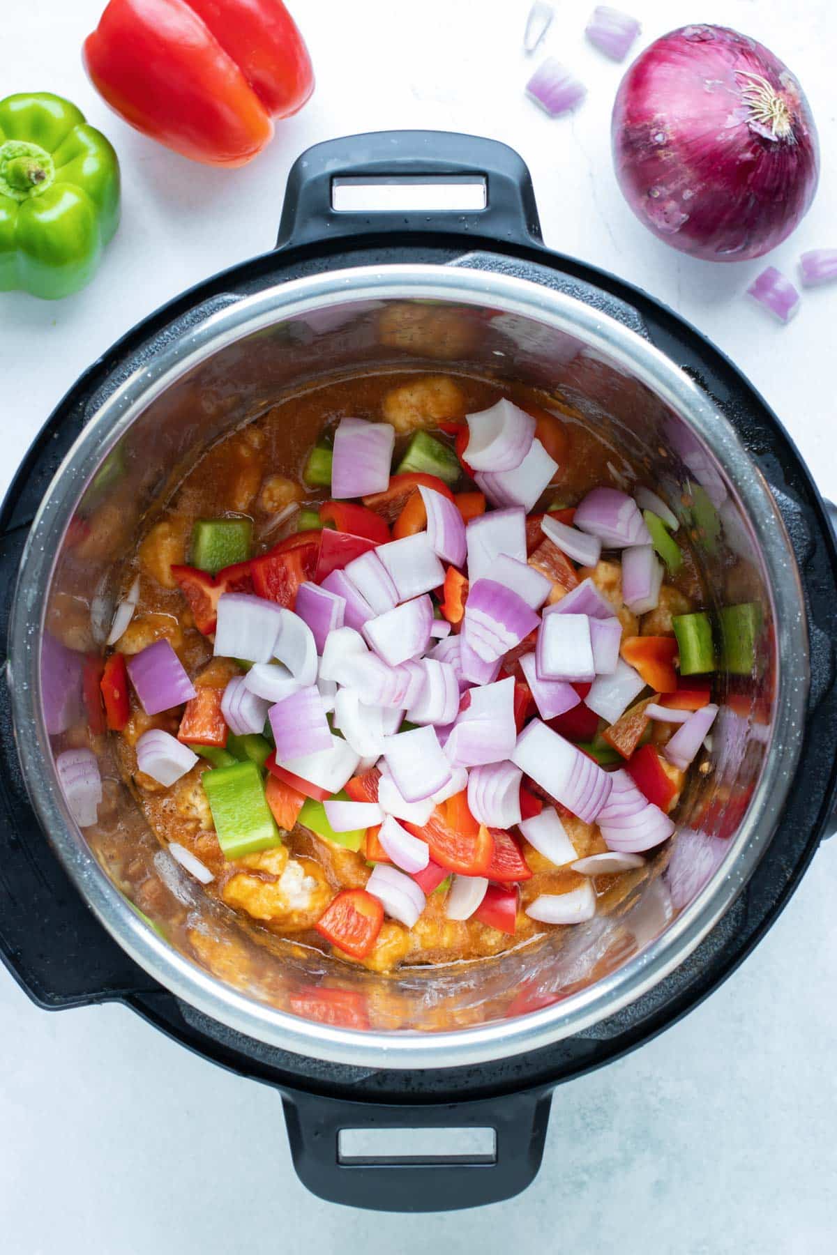 Chopped onions and bell peppers are added to chicken and sauce for Instant Pot Hawaiian Chicken.