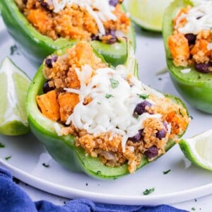 Three stuffed bell peppers are served on a white plate with lime.