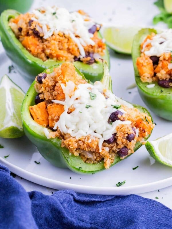 Three stuffed bell peppers are served on a white plate with lime.