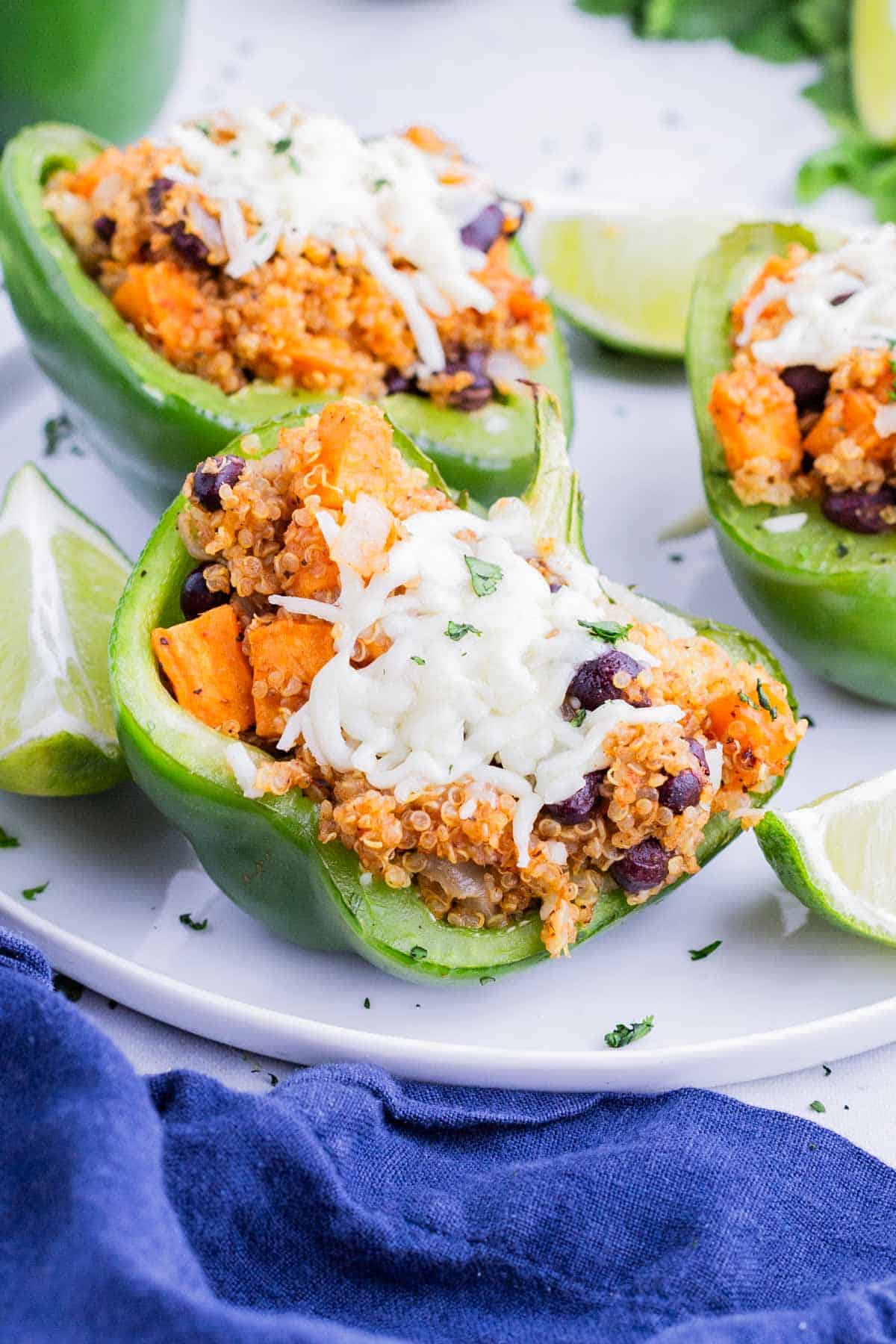 Three stuffed bell peppers are served on a white plate with lime.