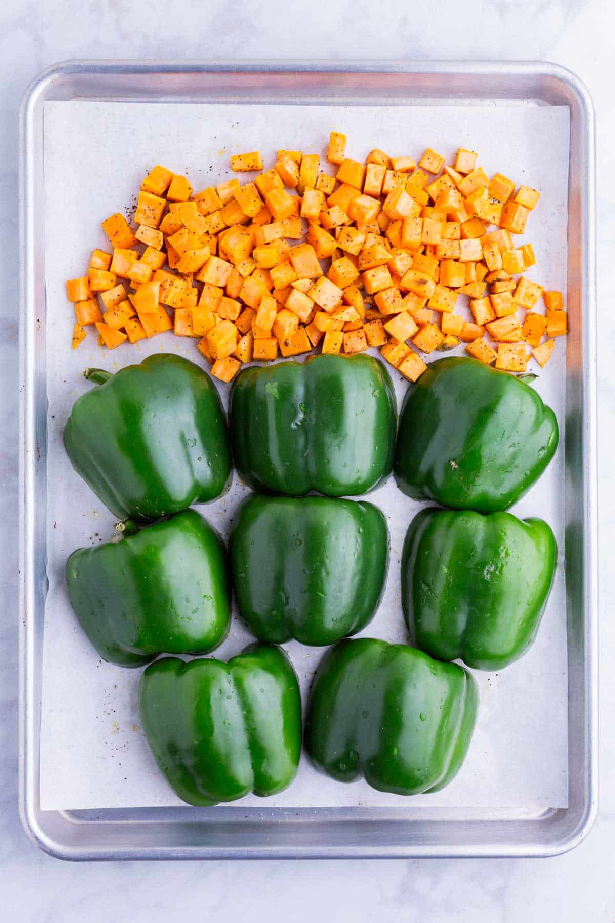 Bell peppers are added to the baking sheet with the sweet potatoes.