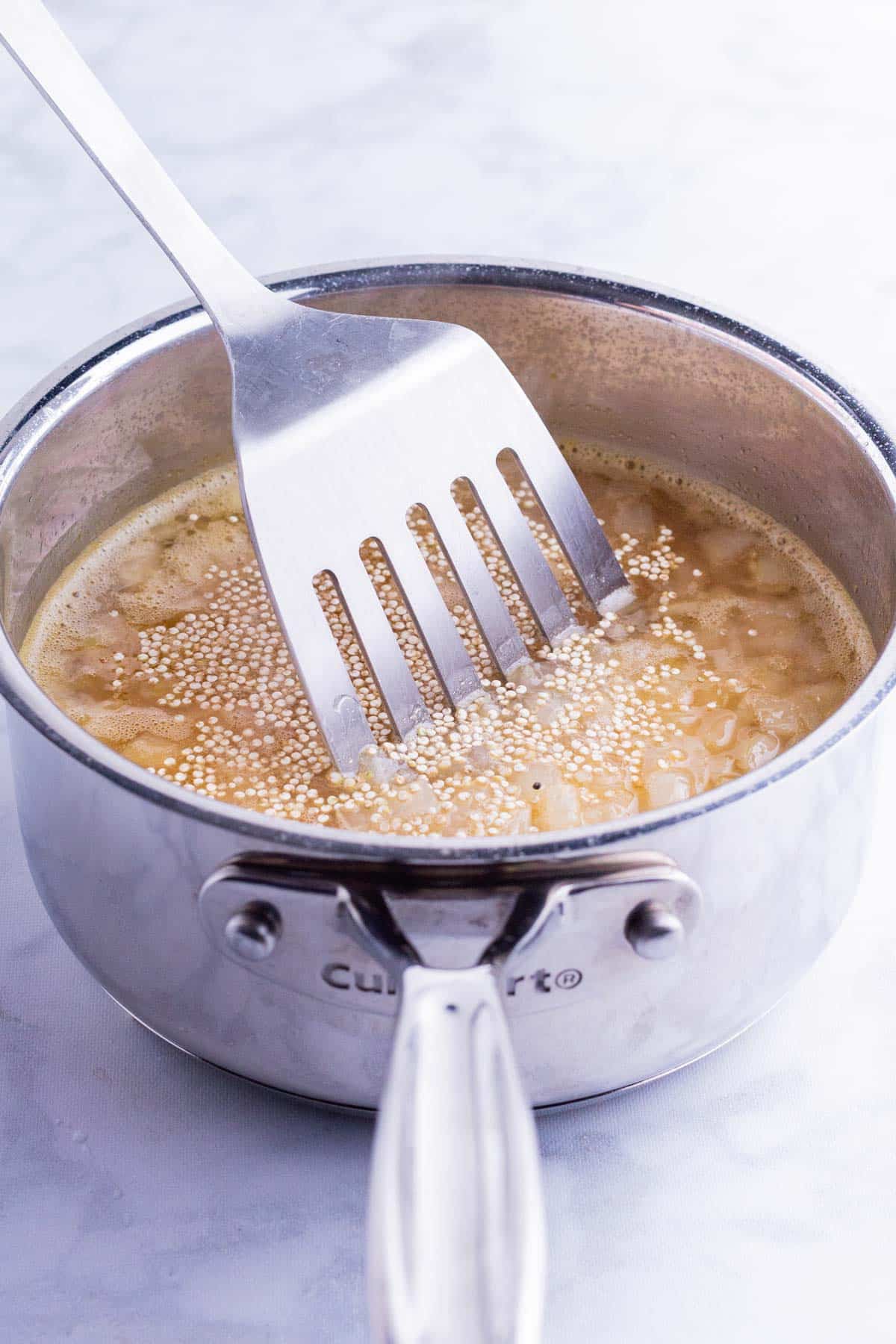A spatula stirs the broth and quinoa into the pot.