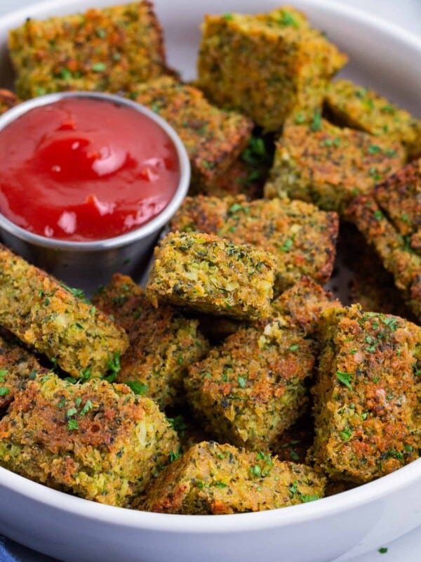 A plate full of cheesy broccoli tots are served with ketchup.