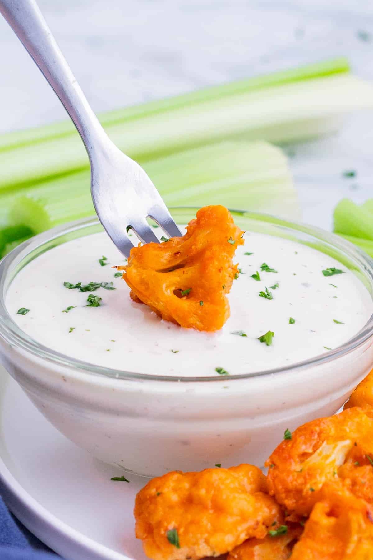 A fork dips a buffalo cauliflower bite into ranch dressing.