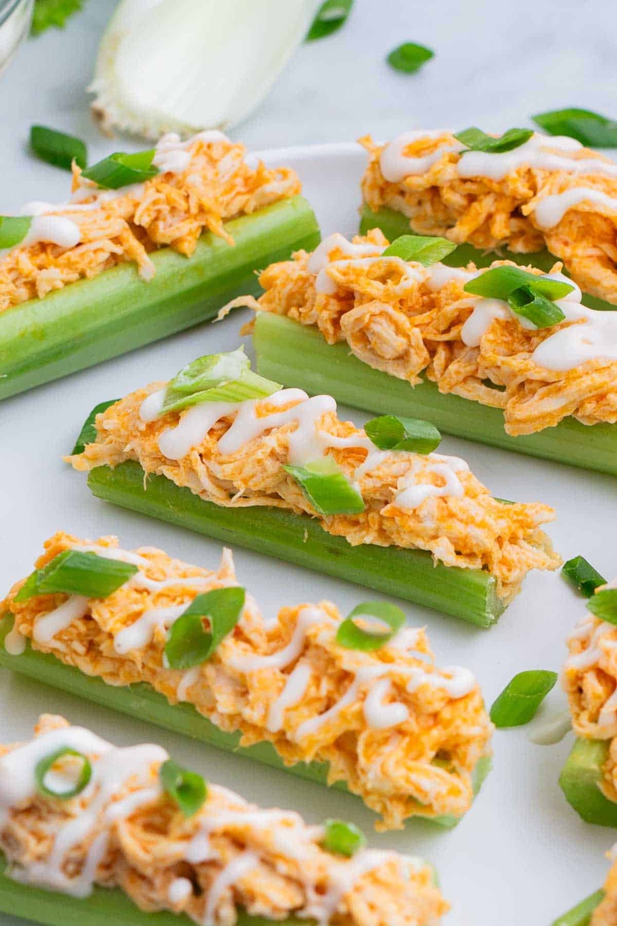 Celery sticks are loaded up with buffalo chicken dip and drizzled with ranch dressing and green onions.