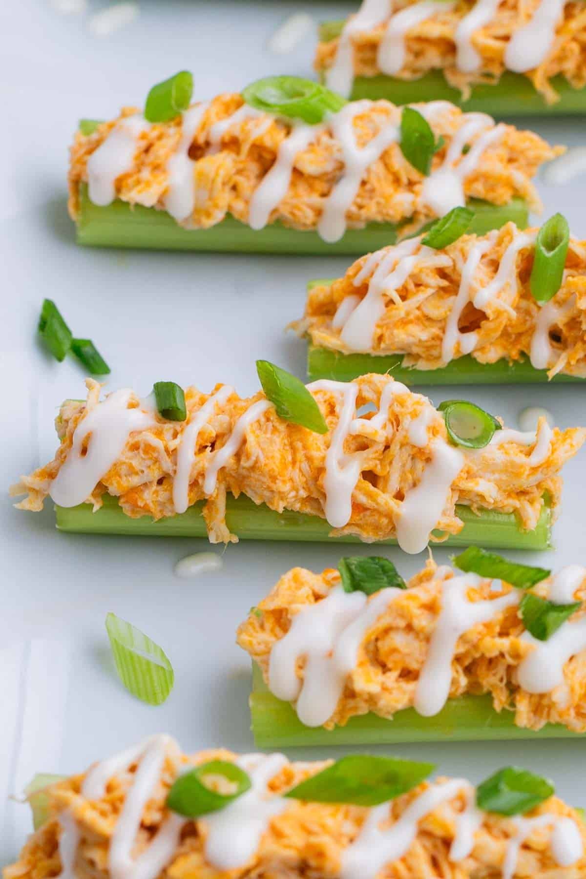 Celery sticks are loaded up with buffalo chicken dip and drizzled with ranch dressing and green onions.