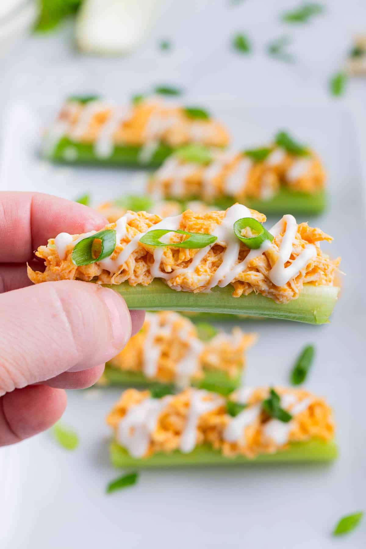A hand holds a piece of celery filled with buffalo chicken dip.