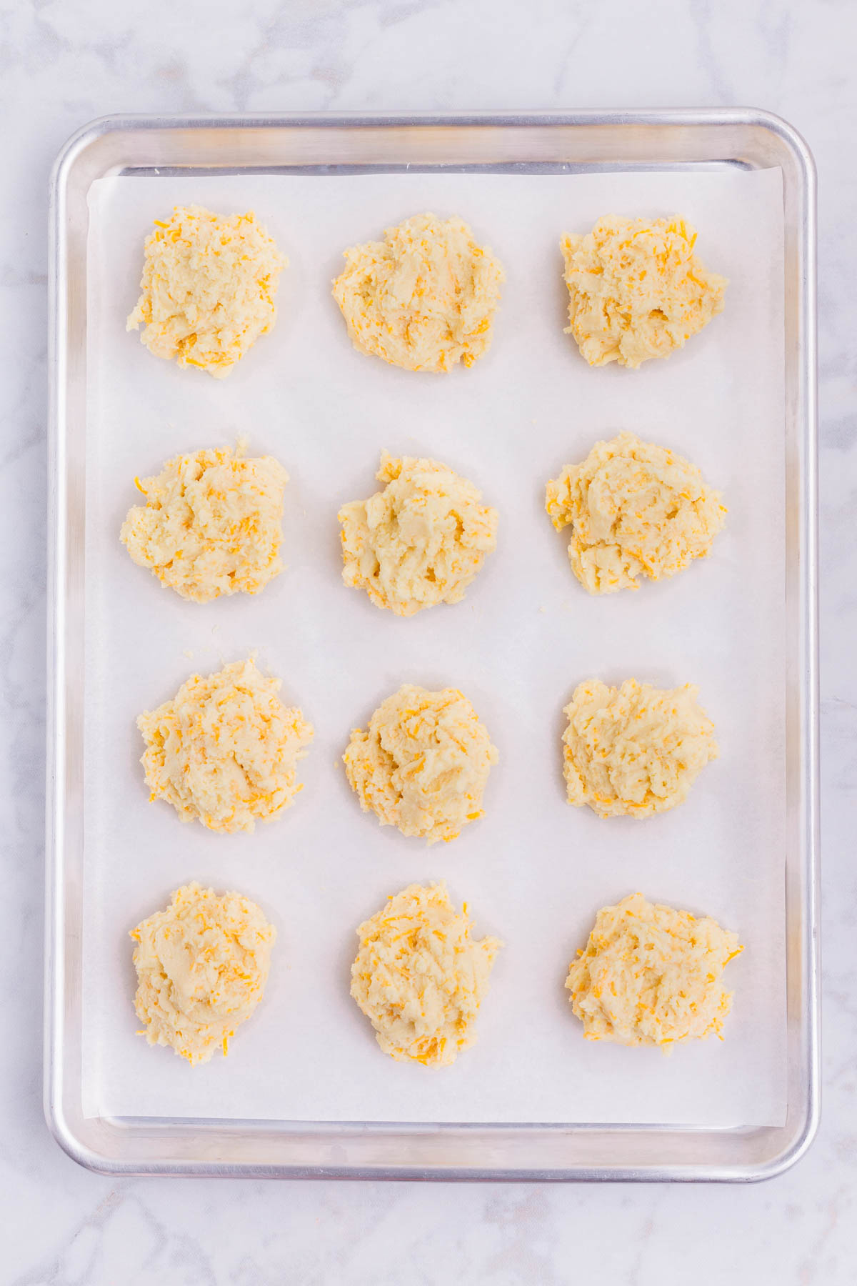 12 biscuits are dropped on a baking sheet lined with parchment paper.