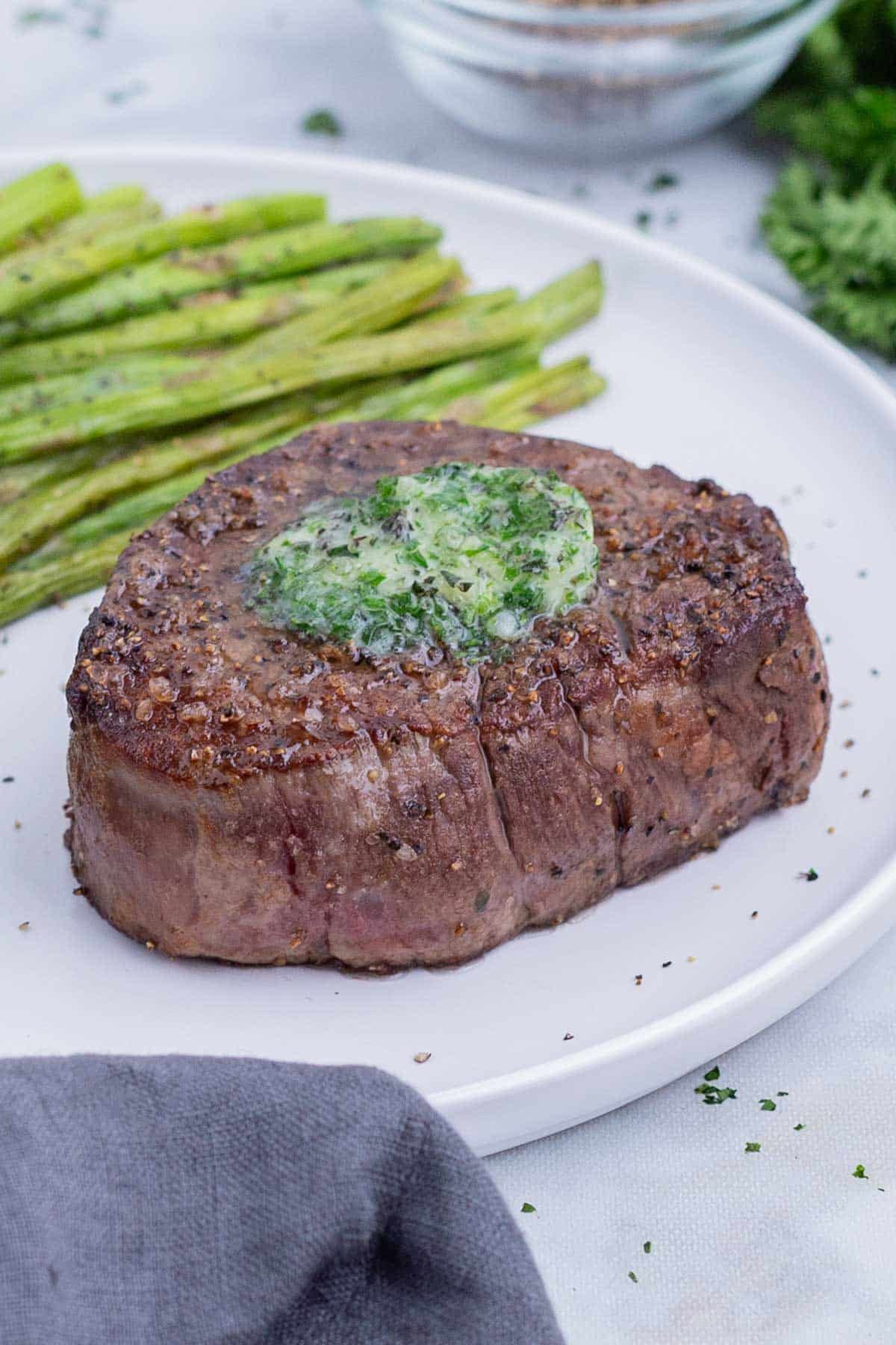 Filet mignon on a white plate with asparagus and herbed butter.