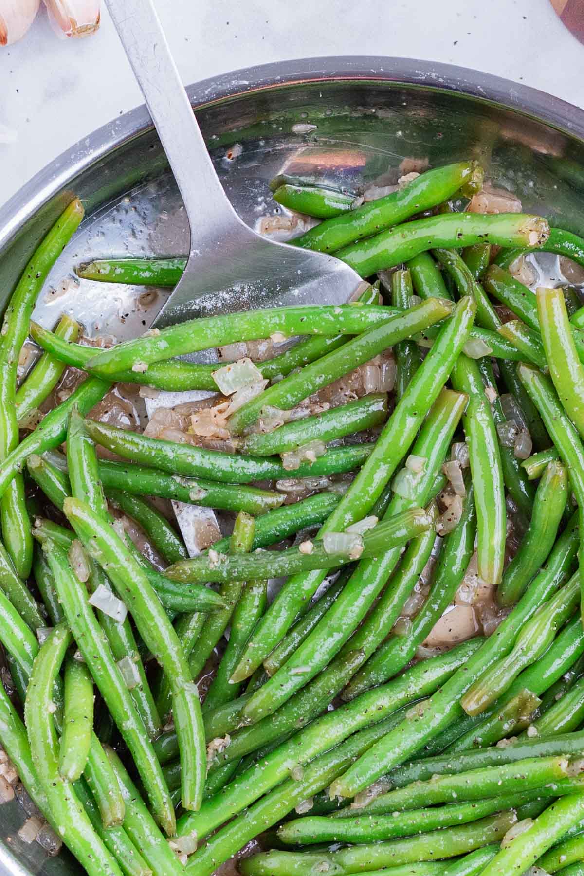 A spatula is used to pick up green beans from a skillet.