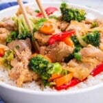 Chopsticks dig into a bowl of honey garlic chicken stir fry over a bed of rice.