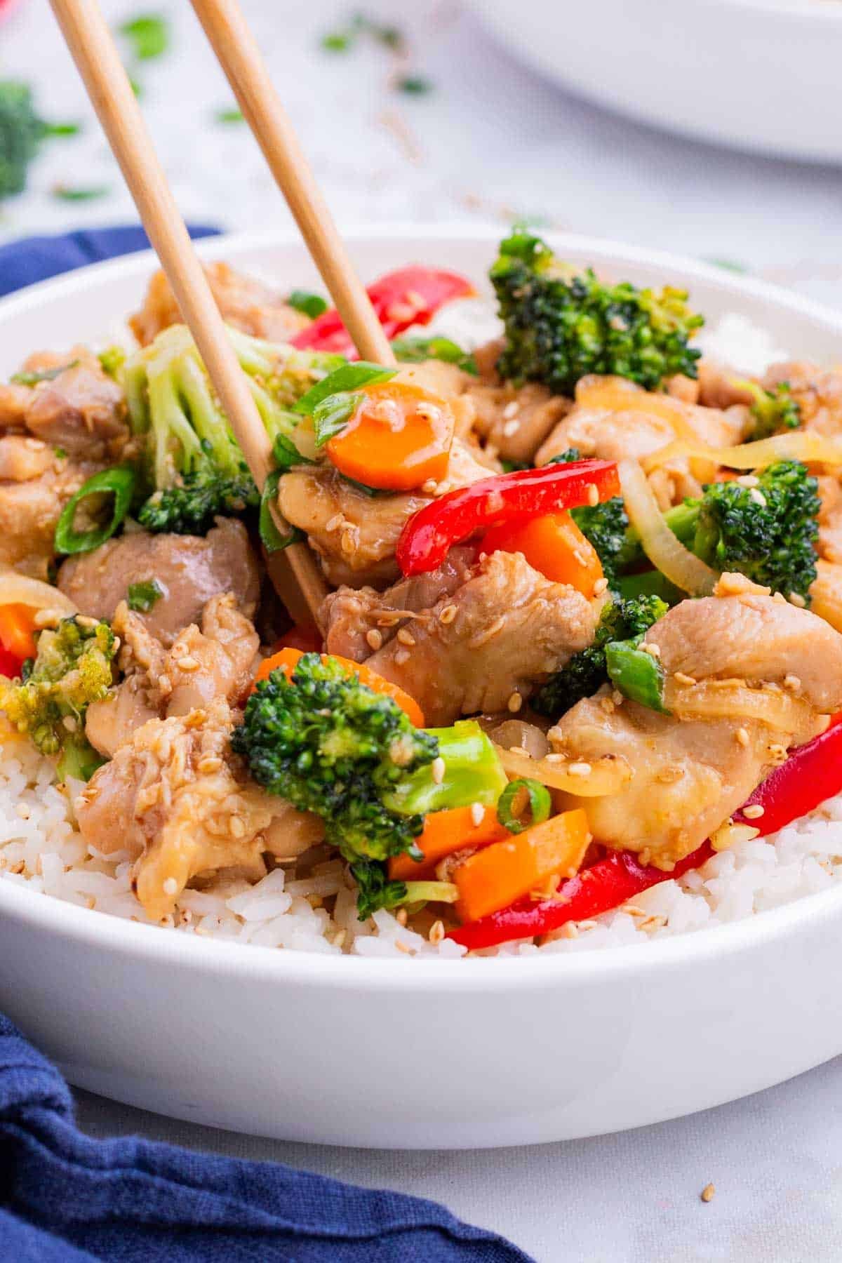 Chopsticks dig into a bowl of honey garlic chicken stir fry over a bed of rice.