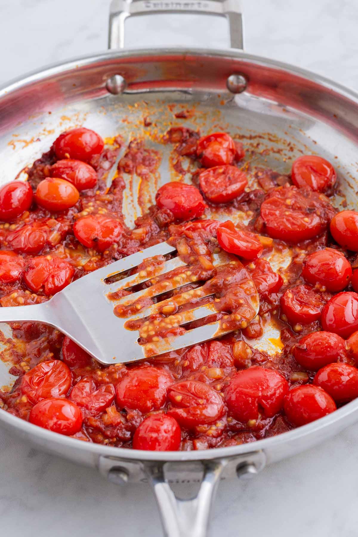 A spatula crushes tomatoes as they cook.